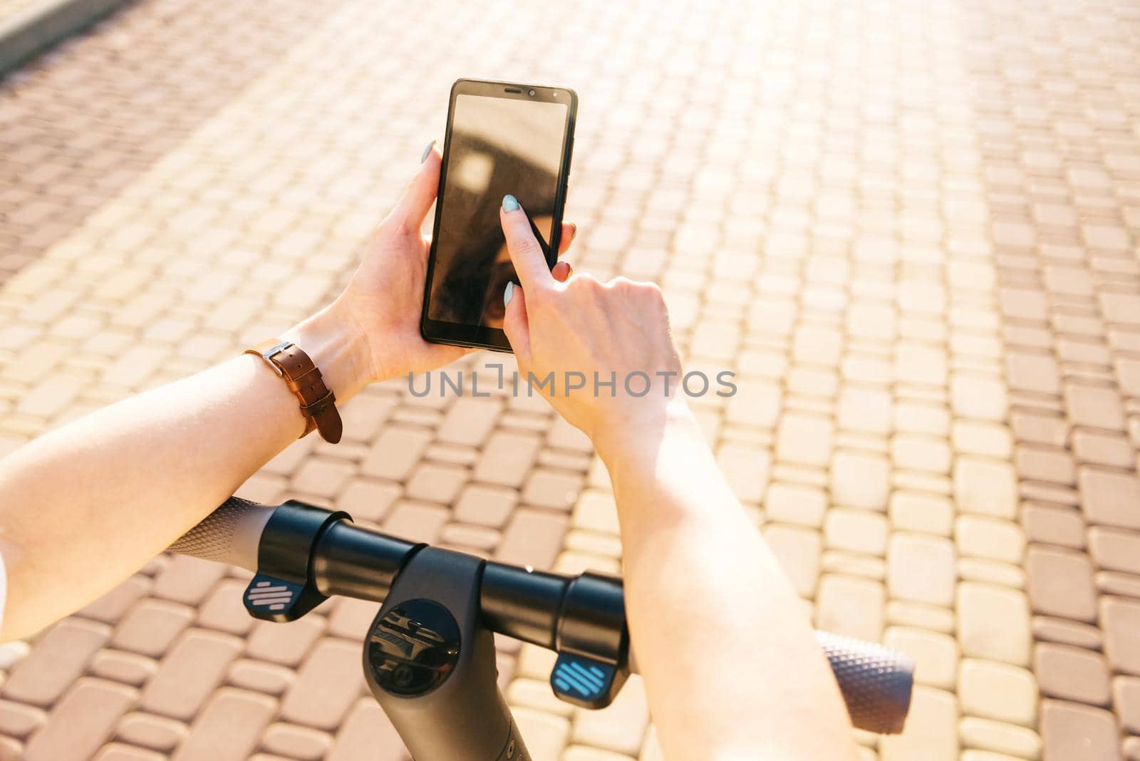 Unrecognizable young woman using smartphone while standing with electric scooter in street outdoor, point of view in first person.