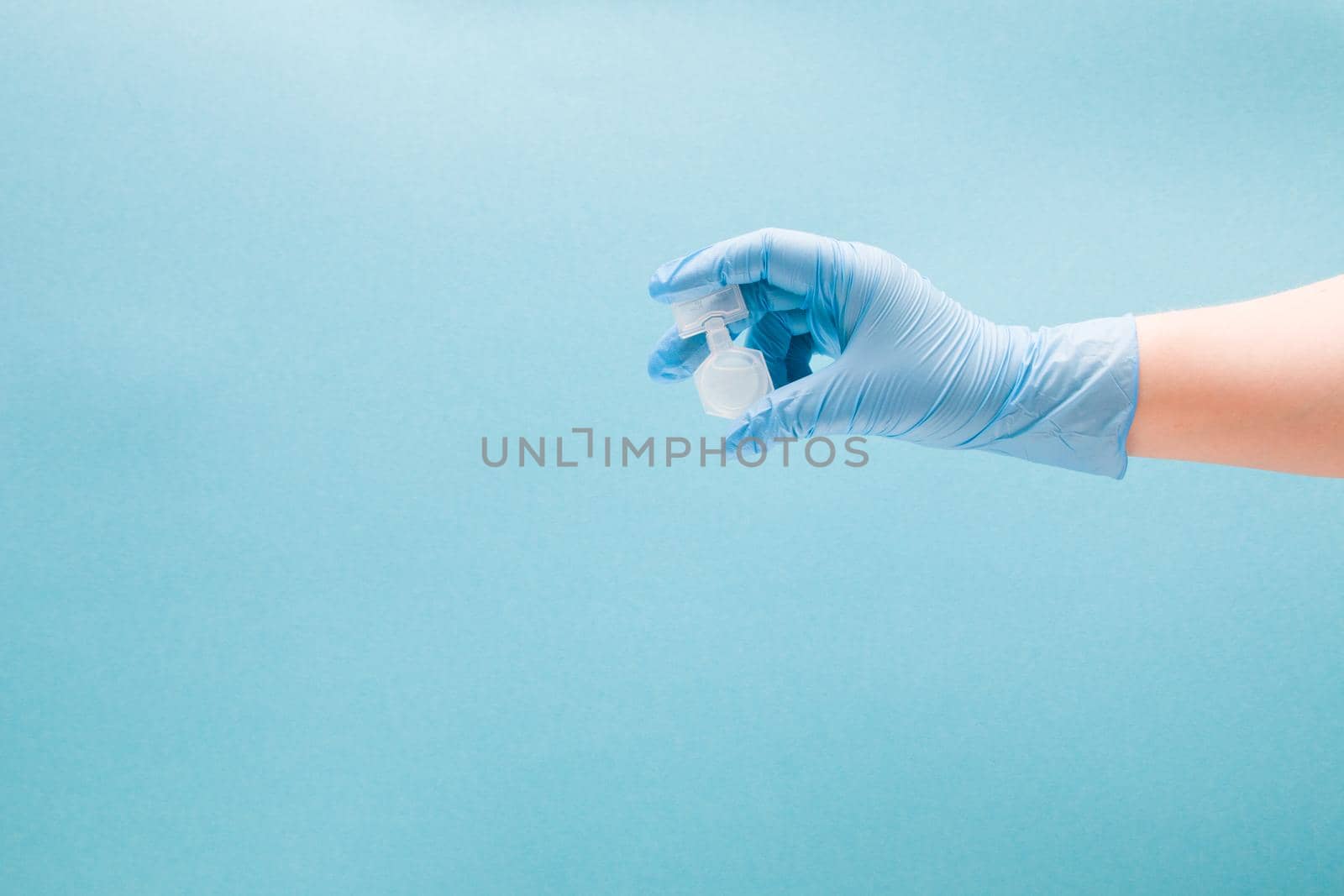 female hand in a blue disposable medical glove holds a container with medication for inhalation in the palm, blue background copy space, treatment of asthma and bronchospasm, pulmonoligia concept