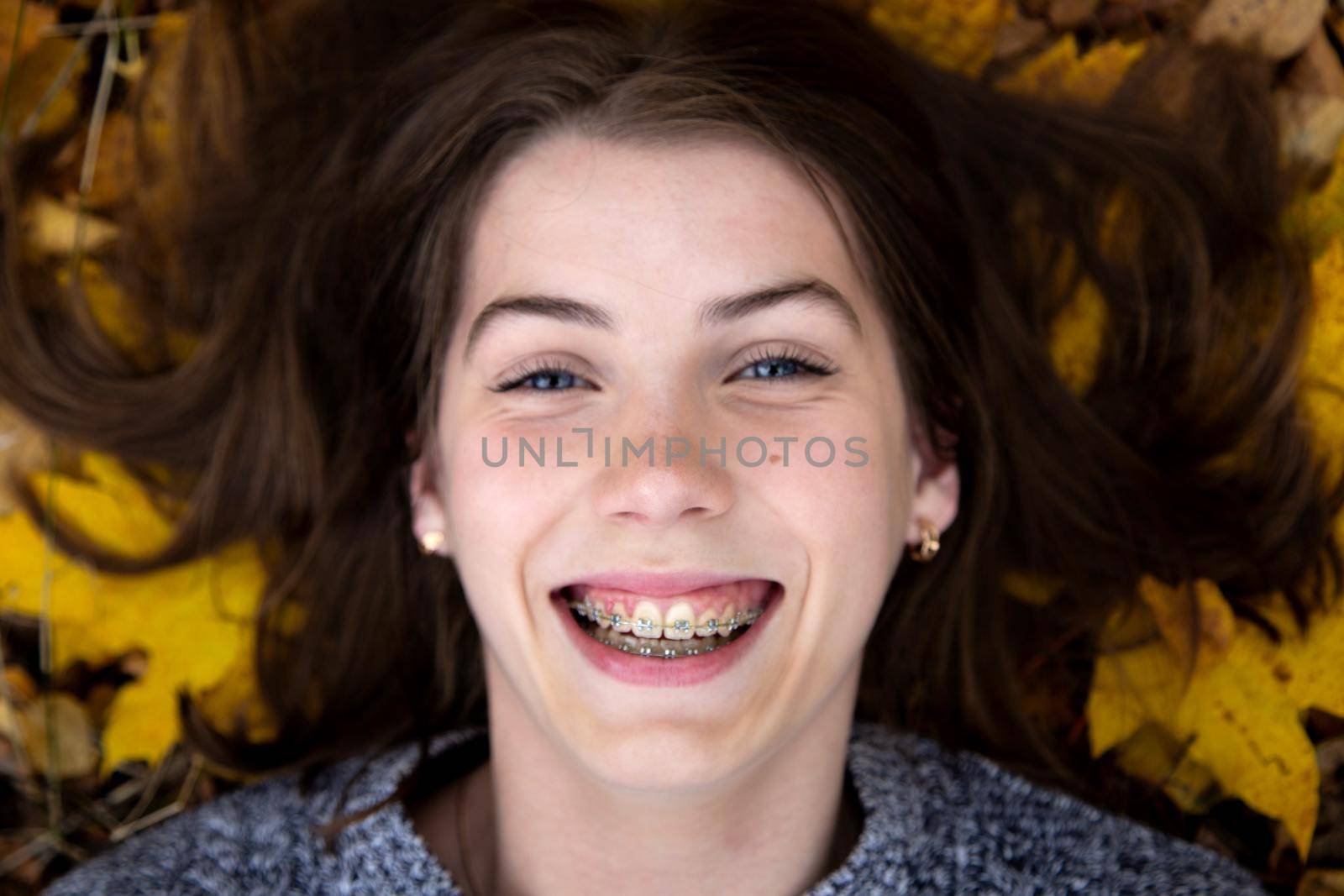 Top view of a pretty girl with blue eyes with a beautiful smile and braces on her teeth, which in the autumn lies on the ground.