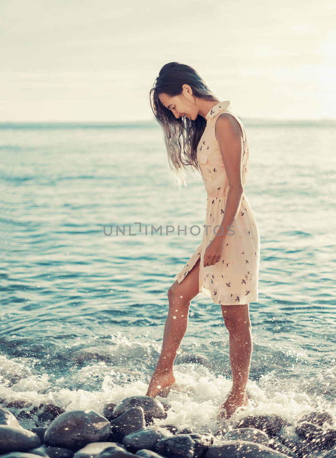 Beautiful young woman walking on pebble beach near the sea. Toned image