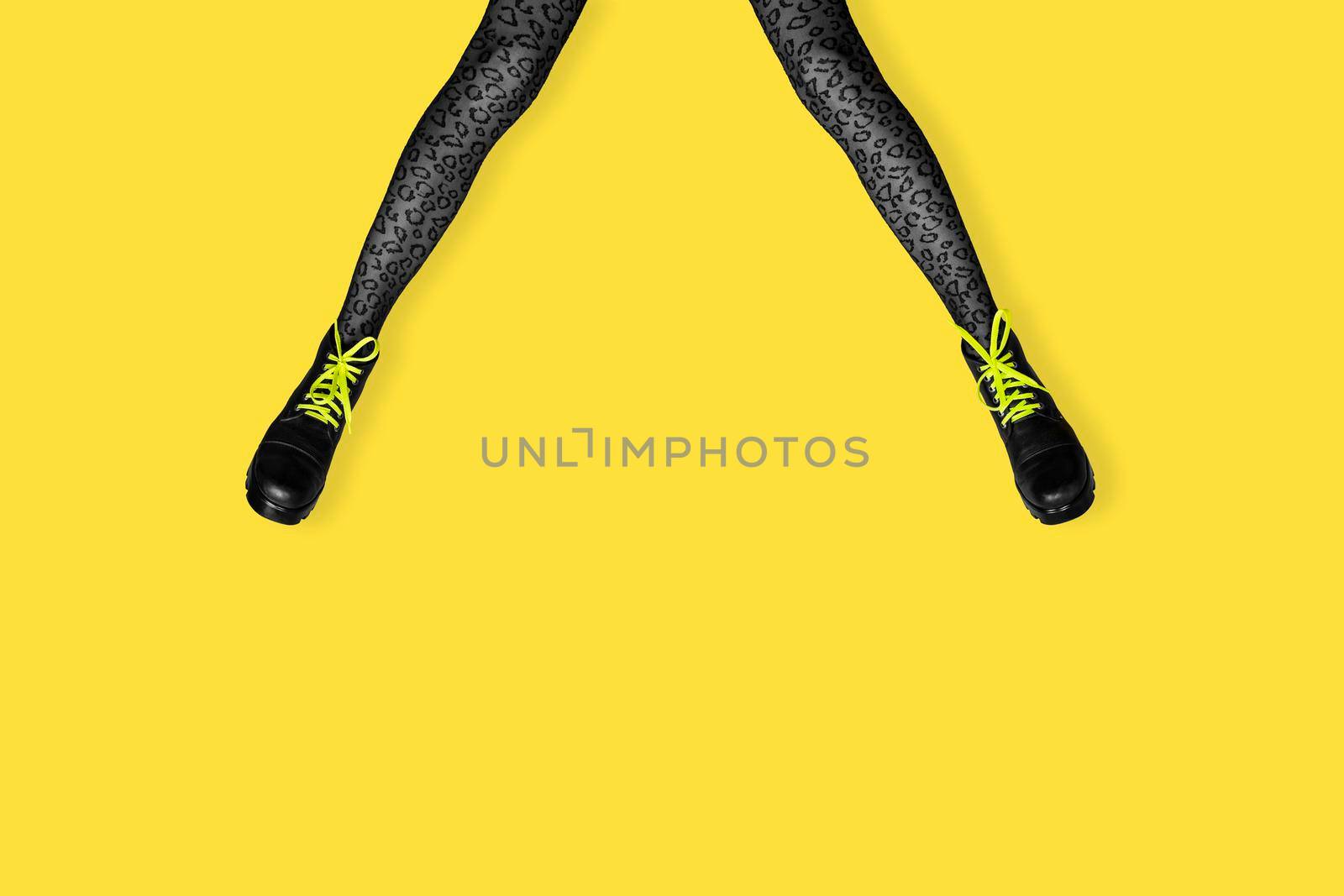 New gray female boots with bright yellow laces on long slender woman legs in gray tiger print tights isolated on yellow background. Pop art concept banner with copy space.