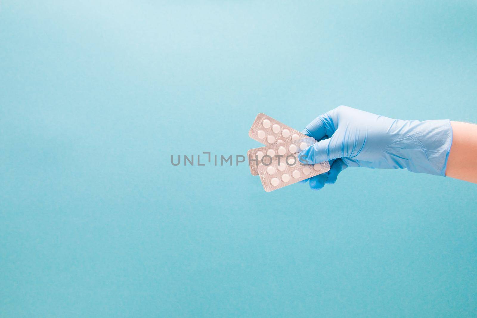 female hand in a blue disposable medical glove holds a fan three blisters with small white tablets on a blue background copy space
