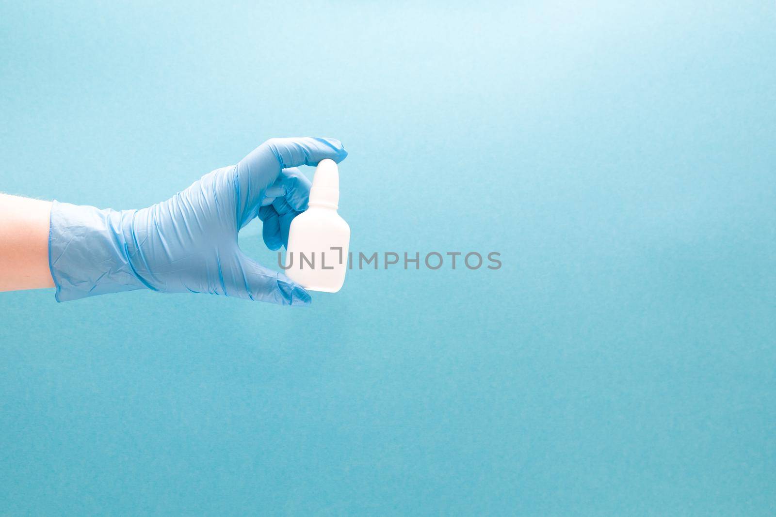 a female hand in a blue disposable medical glove holds a white plastic bottle with drops for the nose without a cap, blue background copy space, nasal drops, medicine for the nose by natashko