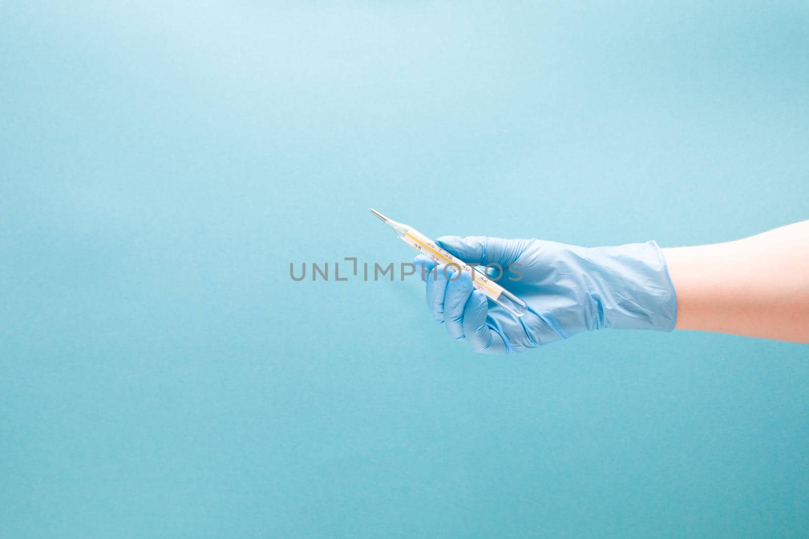 female hand in a blue disposable medical glove holds a mercury thermometer, blue background copy space by natashko