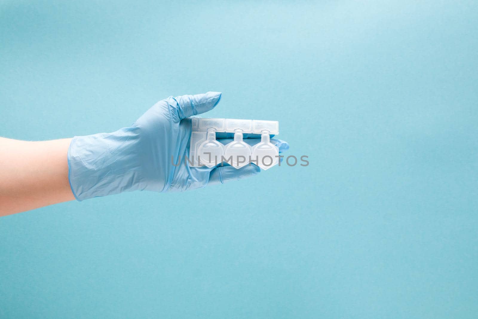 female hand in blue disposable medical glove holds three containers with medication for inhalation in the palm, blue background copy space, treatment of asthma and bronchospasm, pulmonoligia concept