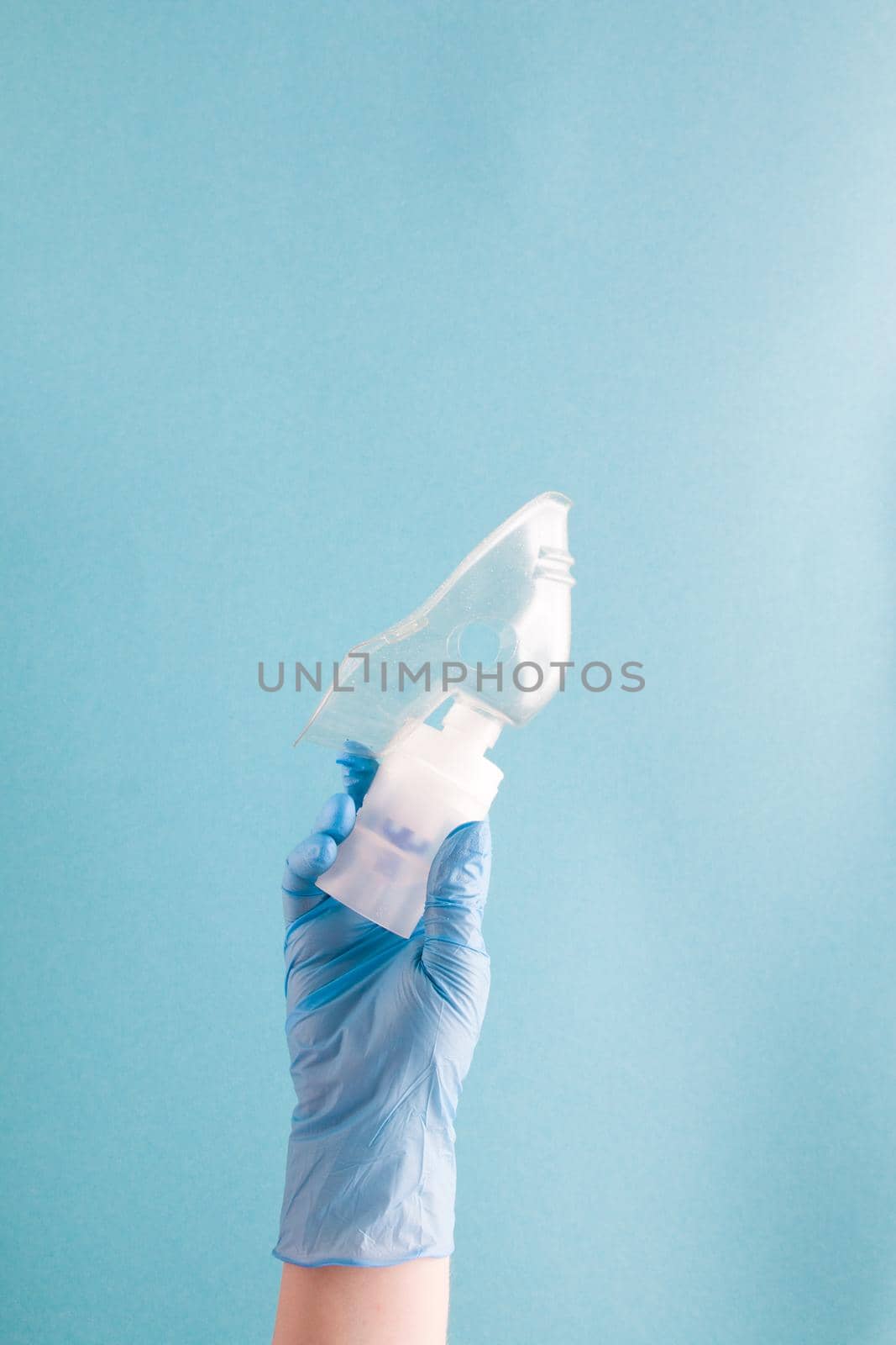 female hand in blue disposable medical glove holds nebulizer drug reservoir with silicone mask, inhalation device, pulmonology concept, blue background, copy space