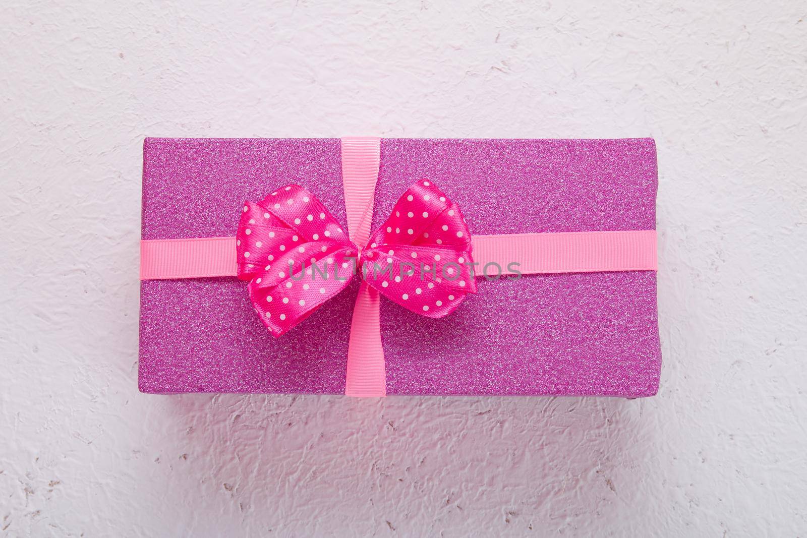 pink shiny gift box on a light white background with pink polka dot bow top view