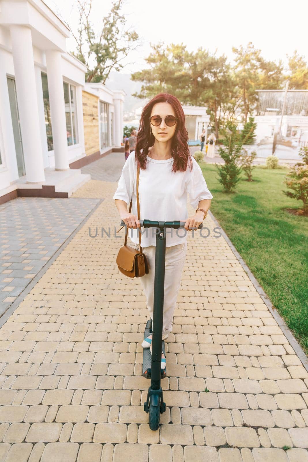 Modern woman riding an eco electric scooter in city park. by alexAleksei