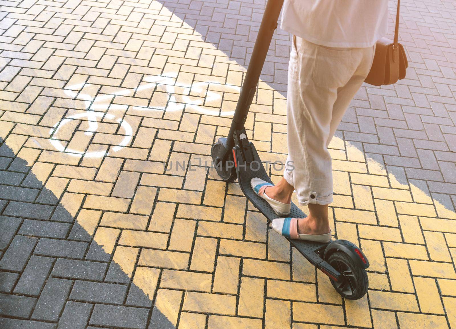 Unrecognizable young woman riding an electric scooter on yellow cycle path, view of legs.