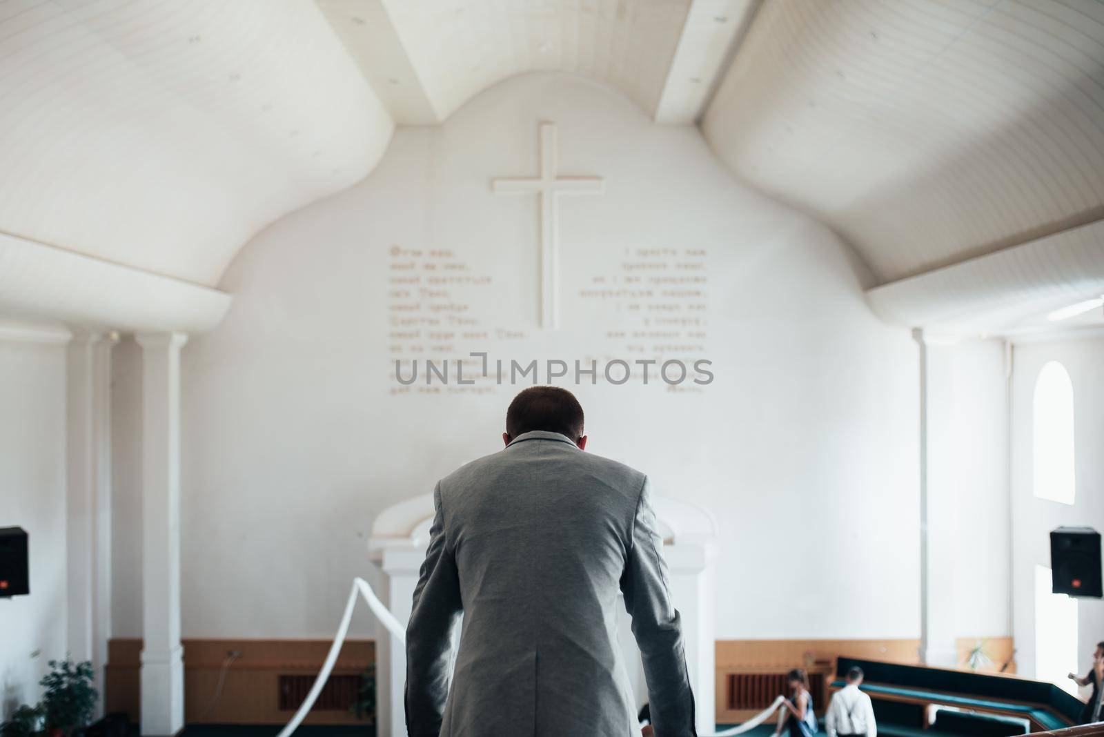 Wedding photo of emotions of a bearded groom with glasses in a gray jacket in the church building by lunarts
