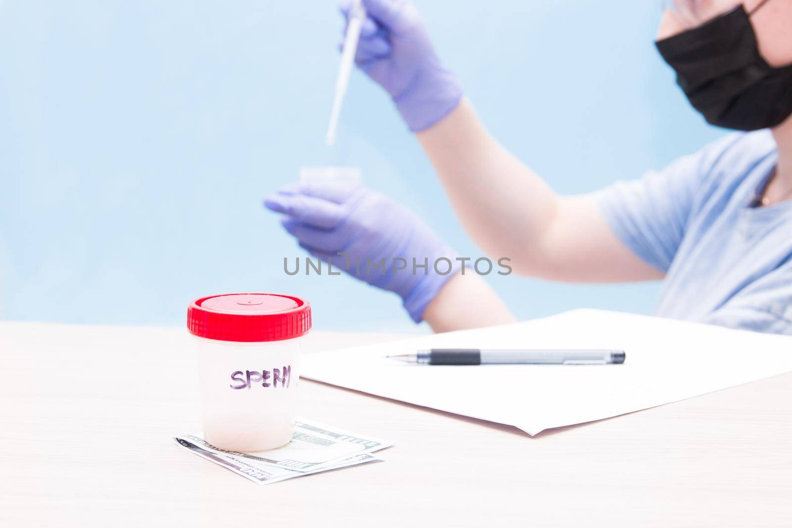 a jar with a red cap with sperm, stand on a banknote of 500 euros, a sperm donor concept, female hands with a pipette and a jar for analysis in the background in blue gloves, blue background, copy space, paper and pen on the table