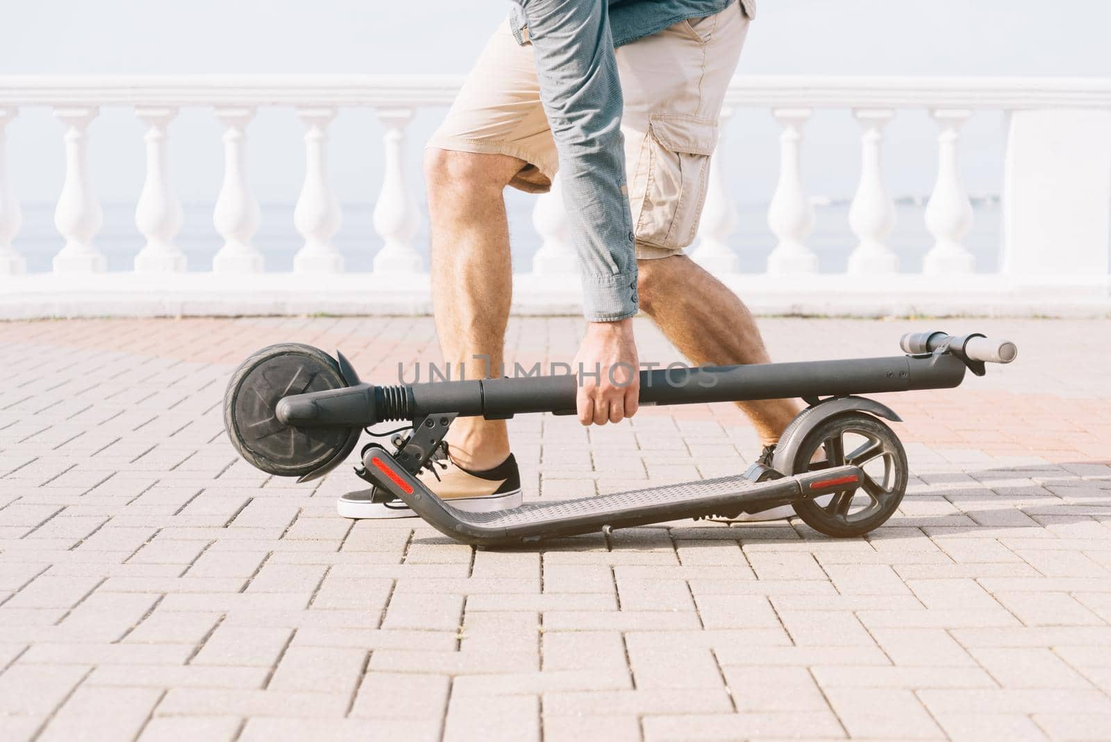 Unrecognizable young man holding folding electric scooter in street outdoor.