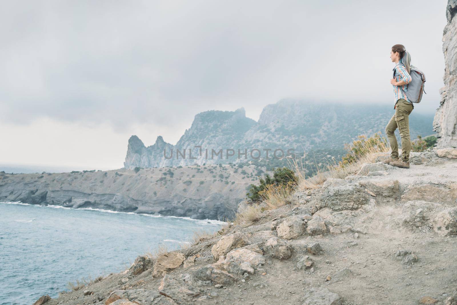 Traveler young woman with backpack standing on high coast and looking at distance