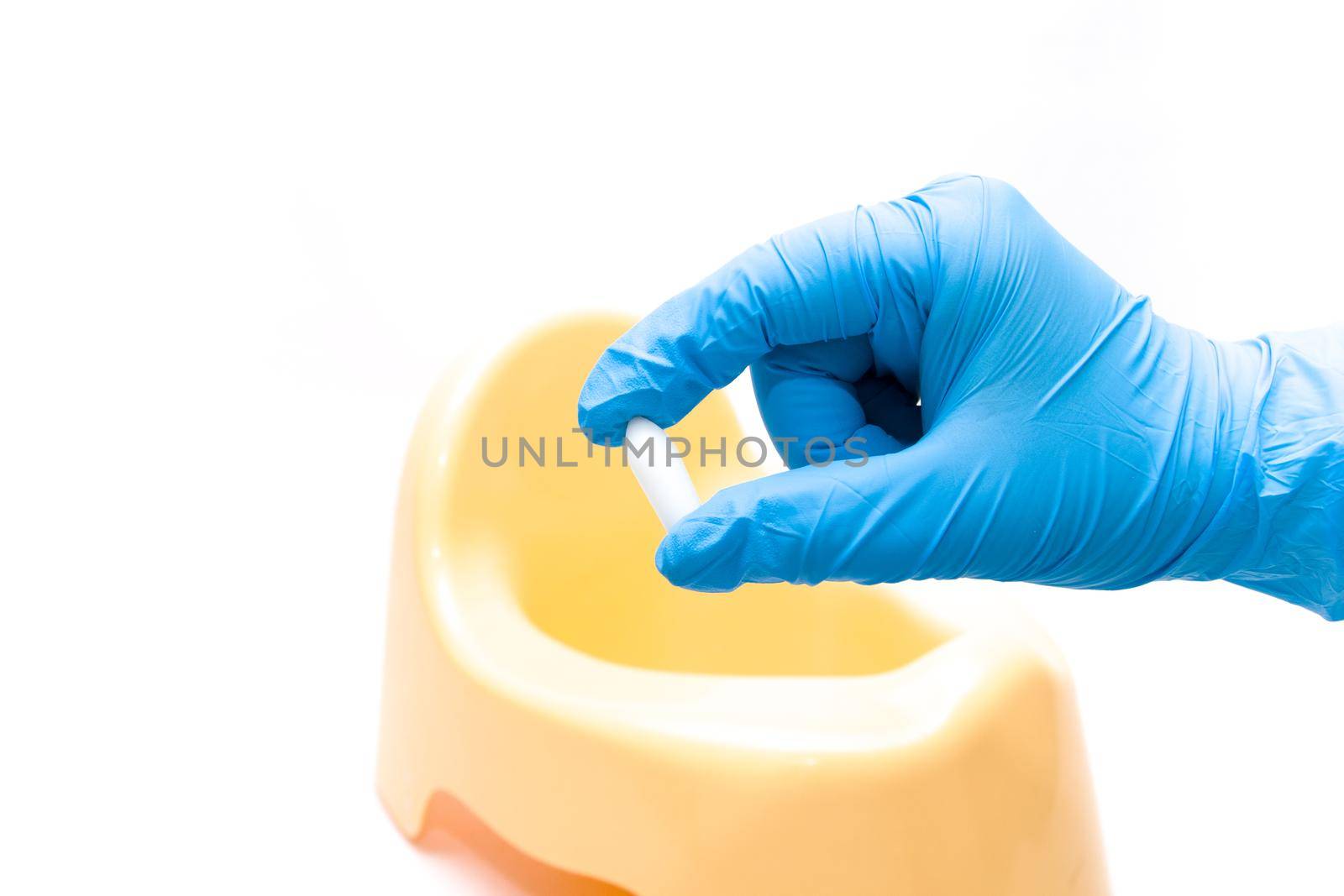 a hand in a disposable blue medical glove holds a test jar with a white spoon for collecting feces, in the background is a yellow children's pot, white background, copy space