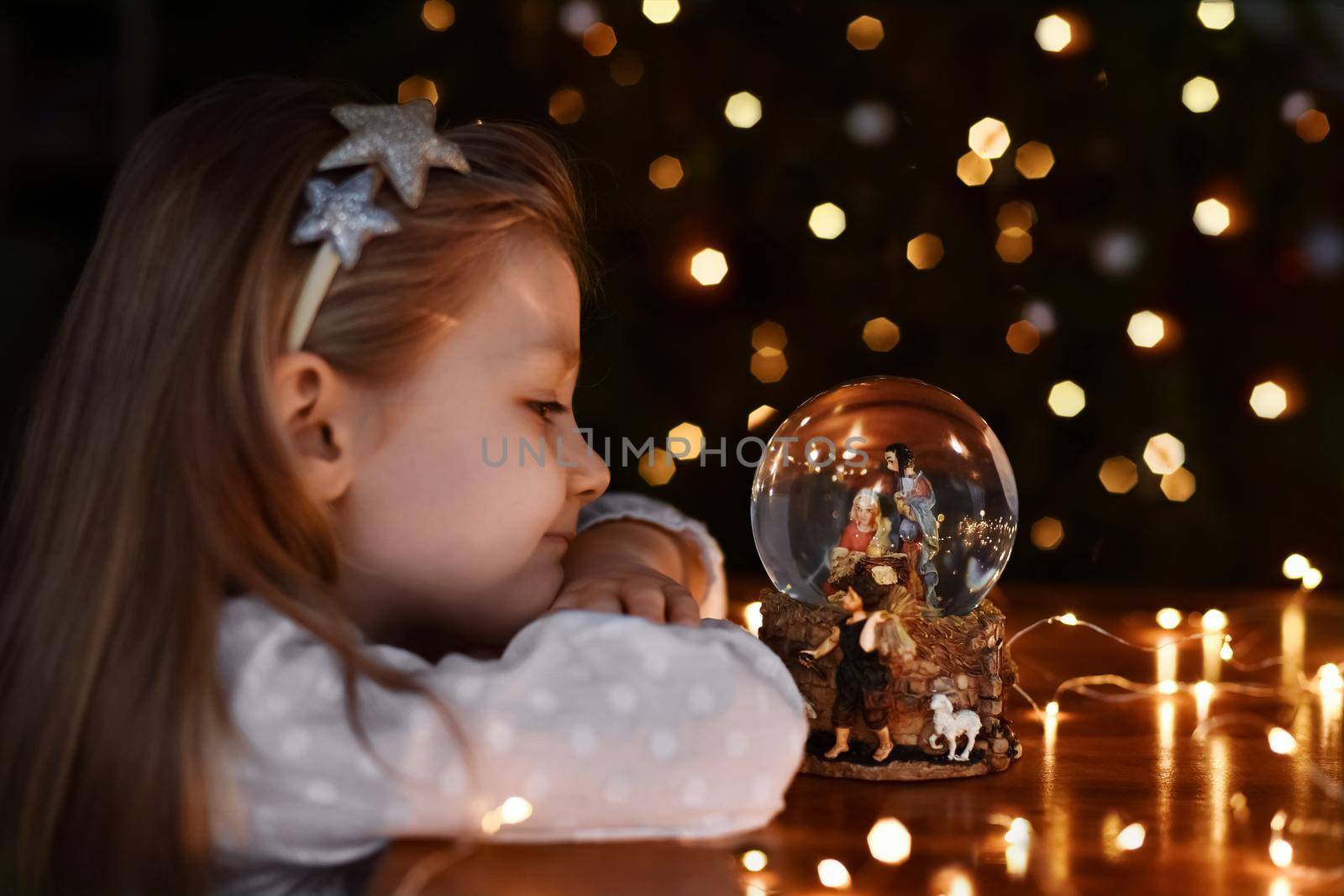 Girl looking at a glass ball with a scene of the birth of Jesus Christ near christmas tree