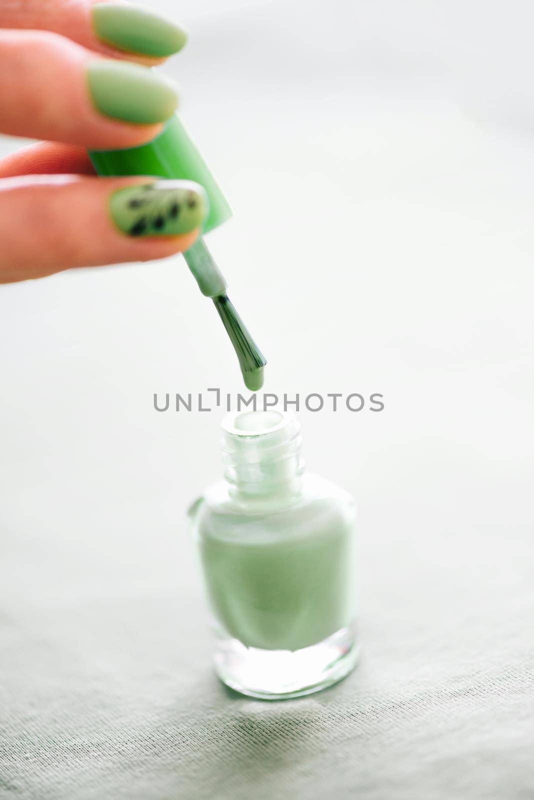 Female hand with manicure holding brush of bottle nail polish green color, close-up.