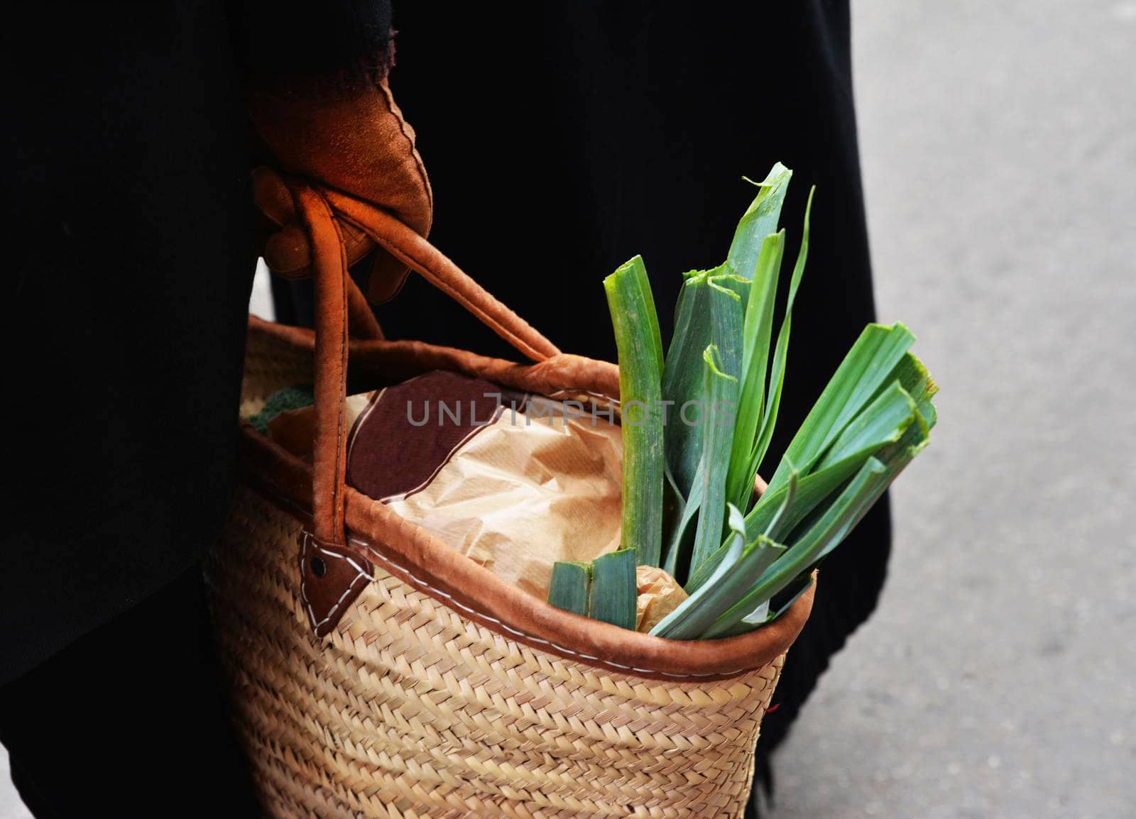 leek in a straw bag in the hands of a woman