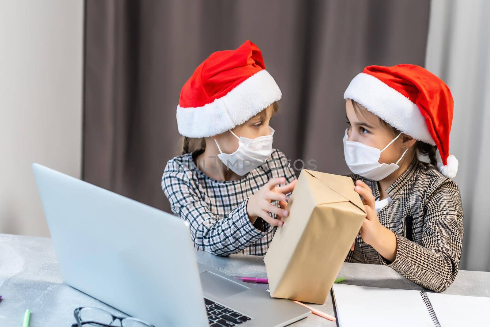 christmas online. two little girls in medical masks are watching a laptop. Concept christmas time