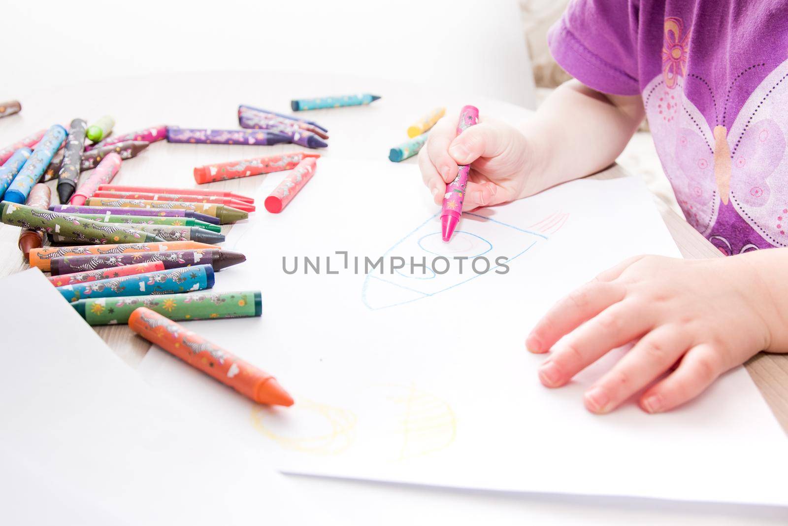 child draws with crayons on paper