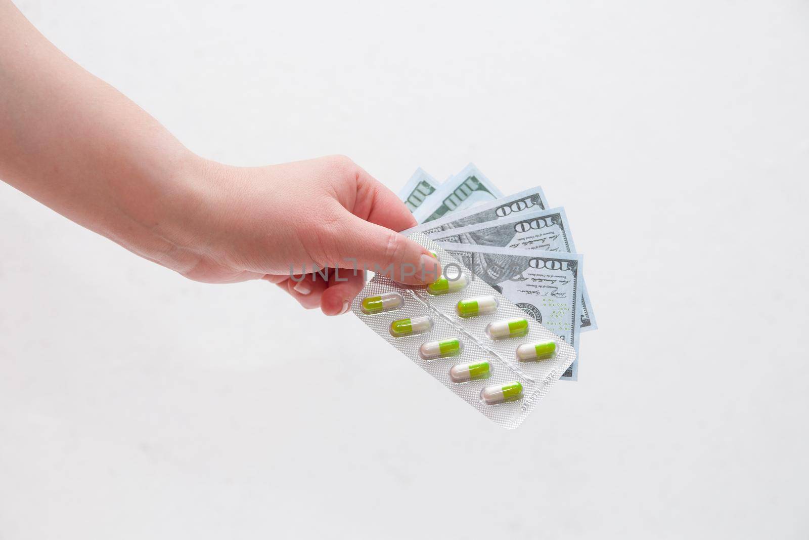 female hands hold a pack of green and white pills capsules medicines and money dollar bills on a white background