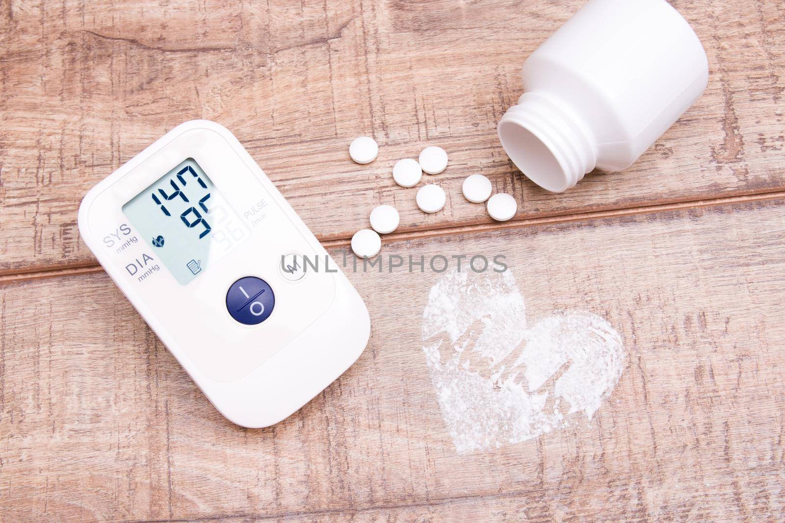 blood pressure monitor and white jar with tablets on a wooden background, heart made of white powder, pulse drawn, copy space, top view, heart pressure concept