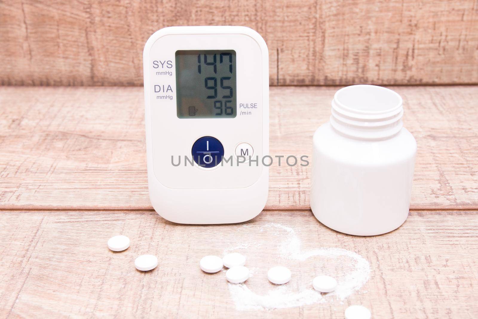 blood pressure monitor and white jar with tablets on a wooden background, heart made of white powder, pulse drawn, copy space, heart pressure concept by natashko