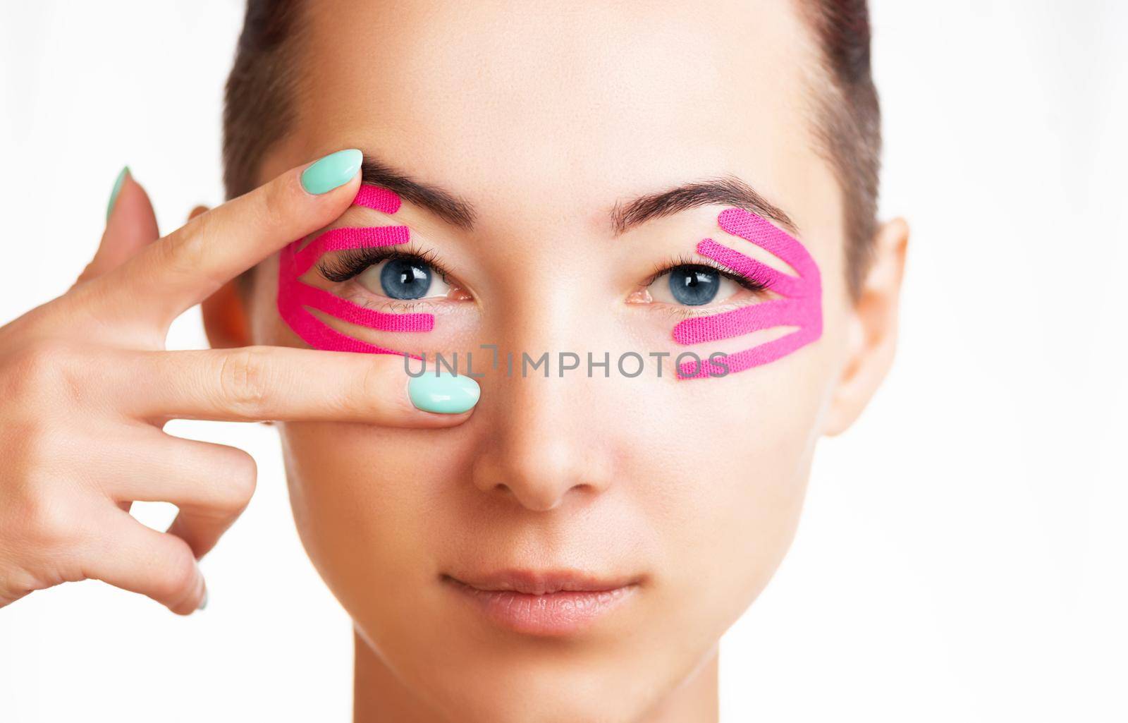 Front view portrait of smiling beautiful young woman with kinesiology tapes on eyelid against wrinkles, anti-aging beauty procedure.