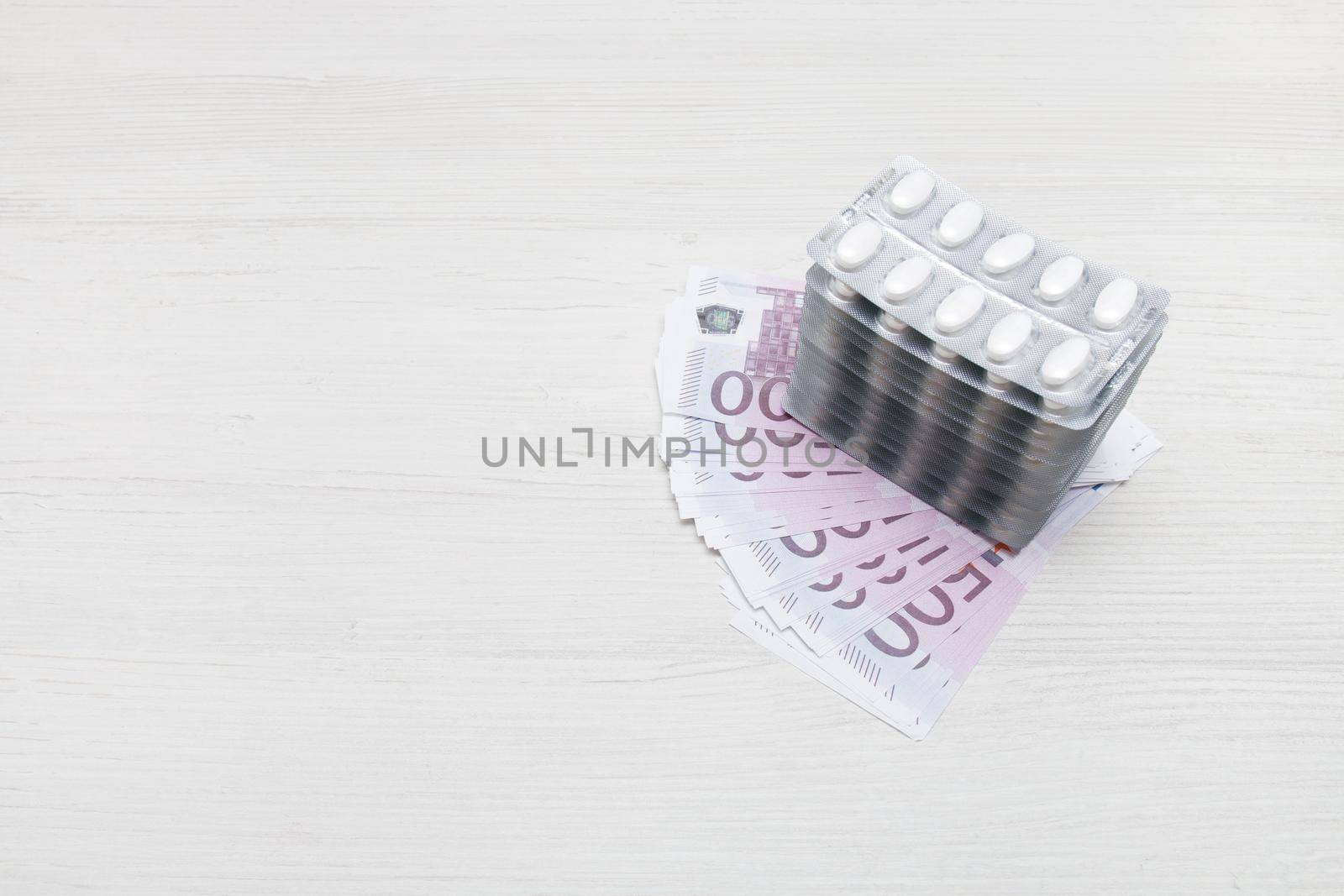 several blisters of tablets on a stack of notes for $ 100, light background, copy space by natashko