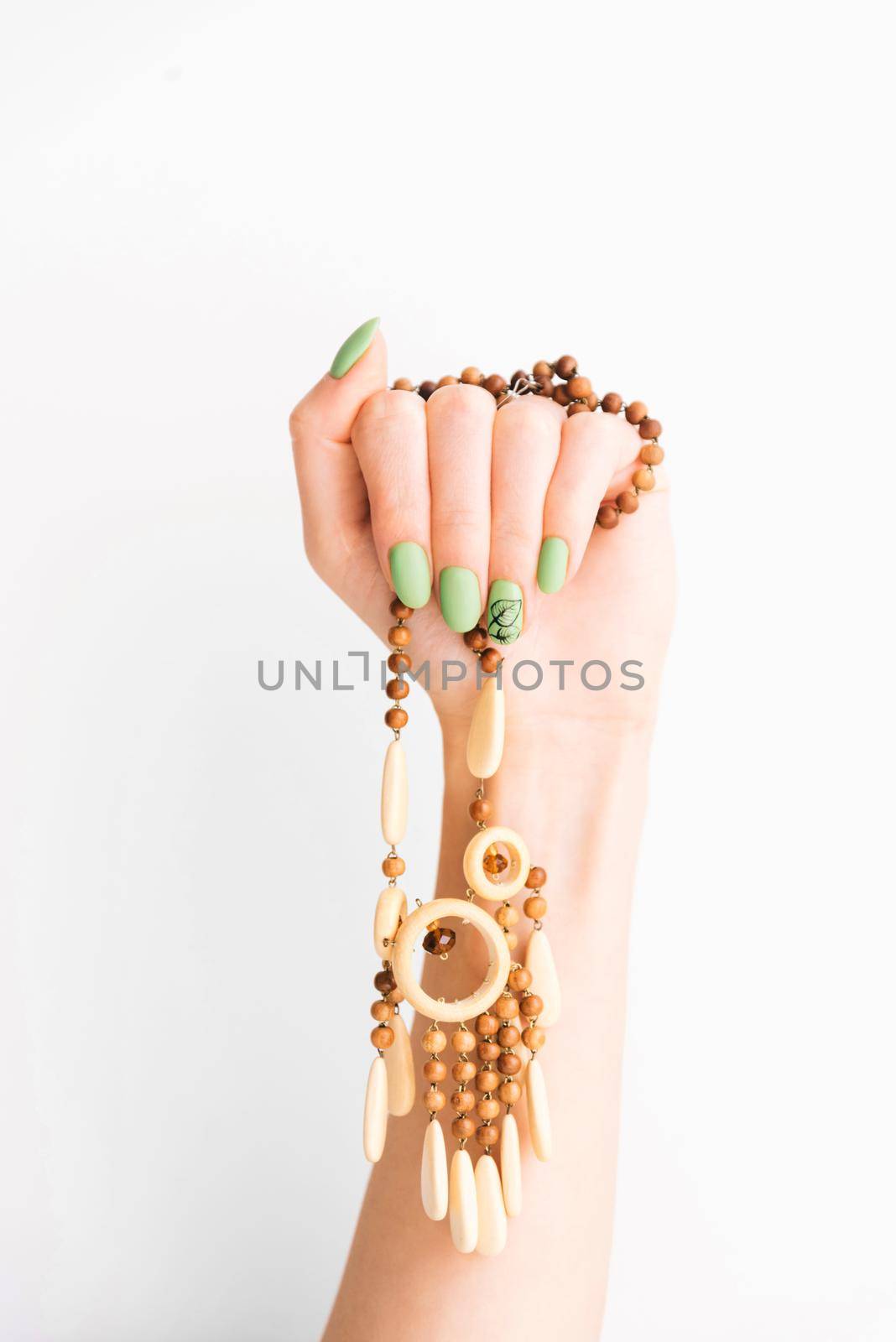 Female hand with green color manicure and art leaf design holding wooden handmade necklace on a white background.