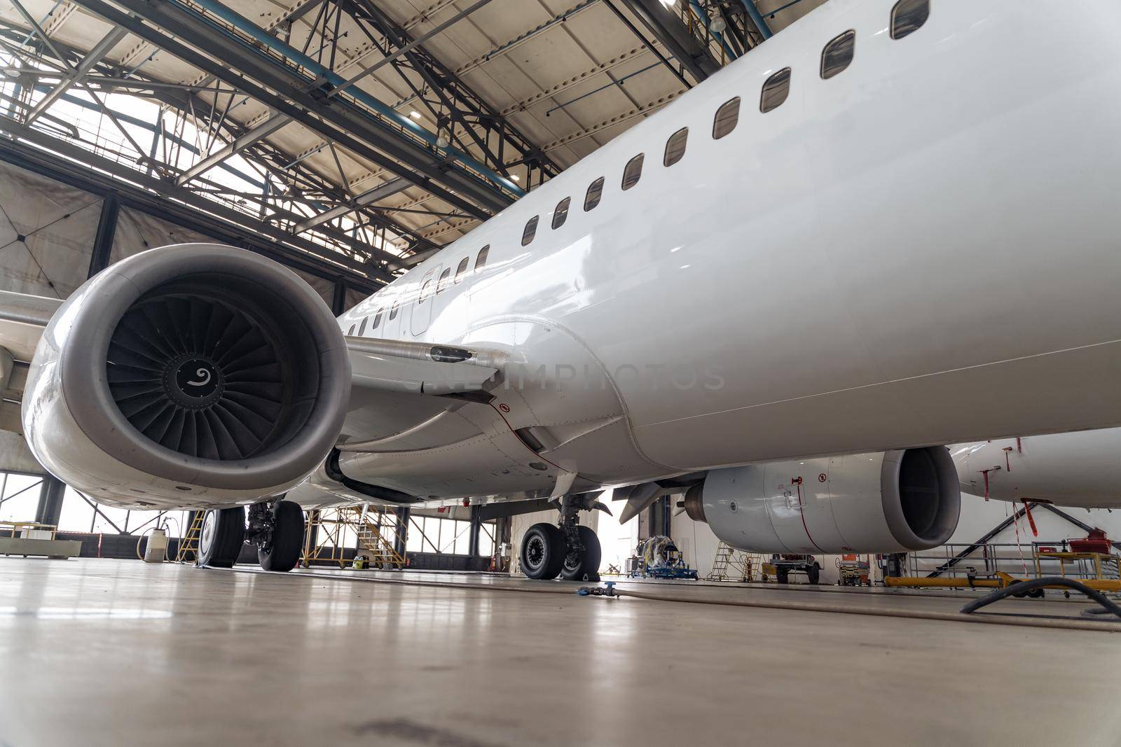 Modern big white passenger airplane on maintenance repair check in airport hangar indoors. Aircraft concept