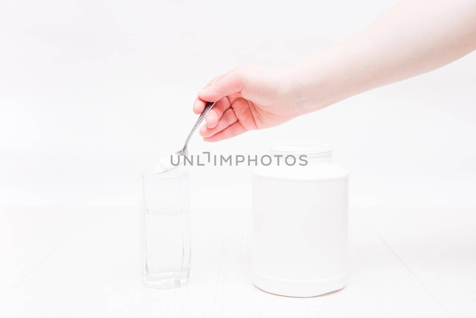 jar and glass of water on a white background, a hand holds a spoon and pours powder into a glass of water, absorbent treatment concept by natashko