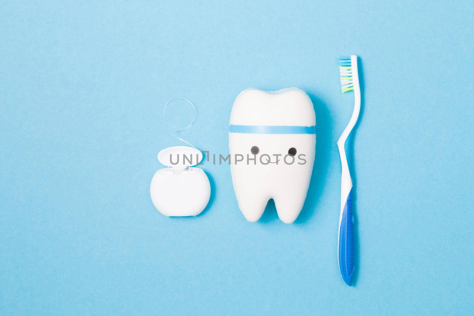 sweets, toothbrush, dental floss and toy tooth on a blue background, tooth model with a smile, protection of the oral cavity from caries concept, pediatric dentistry advertising