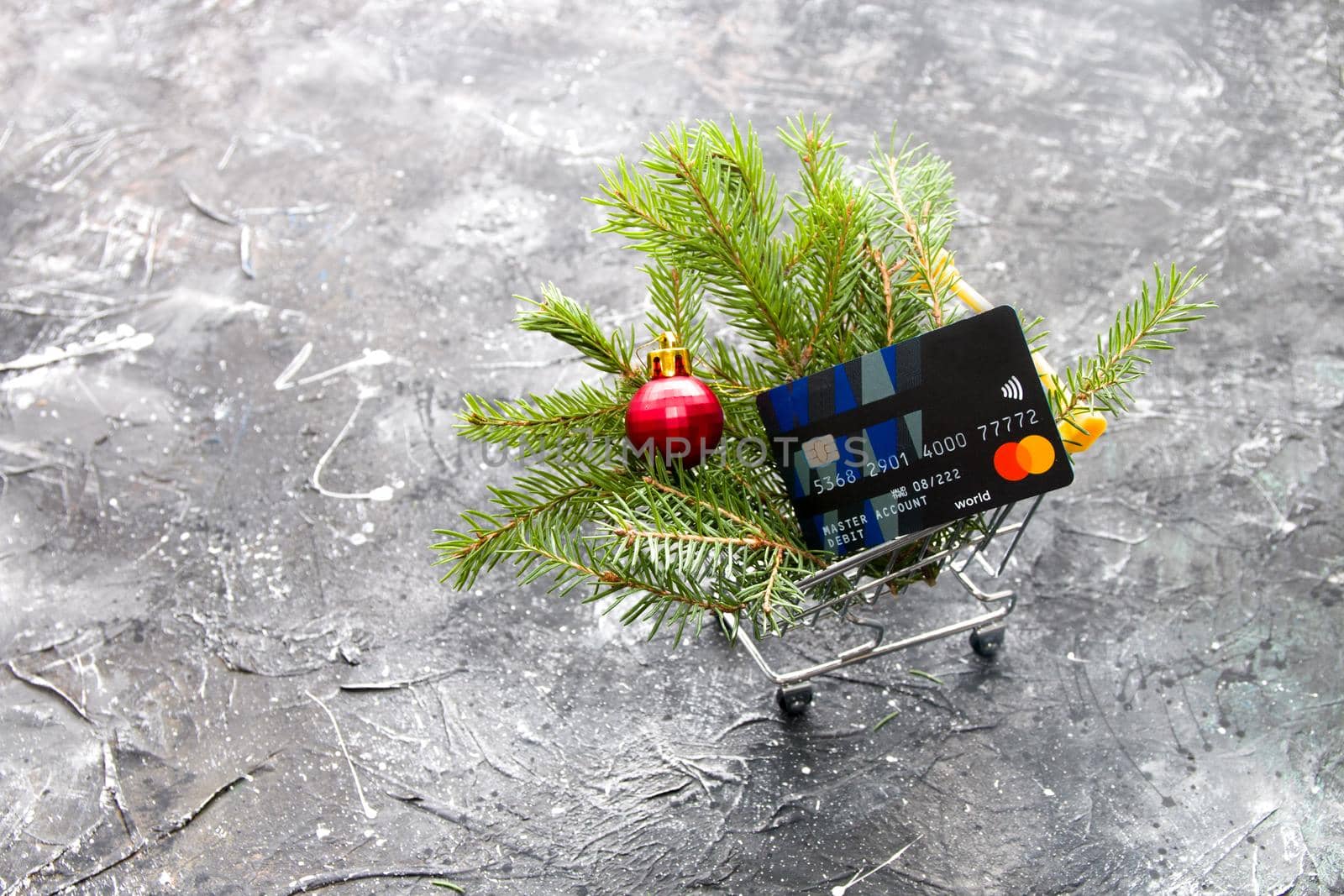 spruce green branch and red shiny Christmas-tree toy ball in a miniature shopping trolley on a black background, copy space by natashko