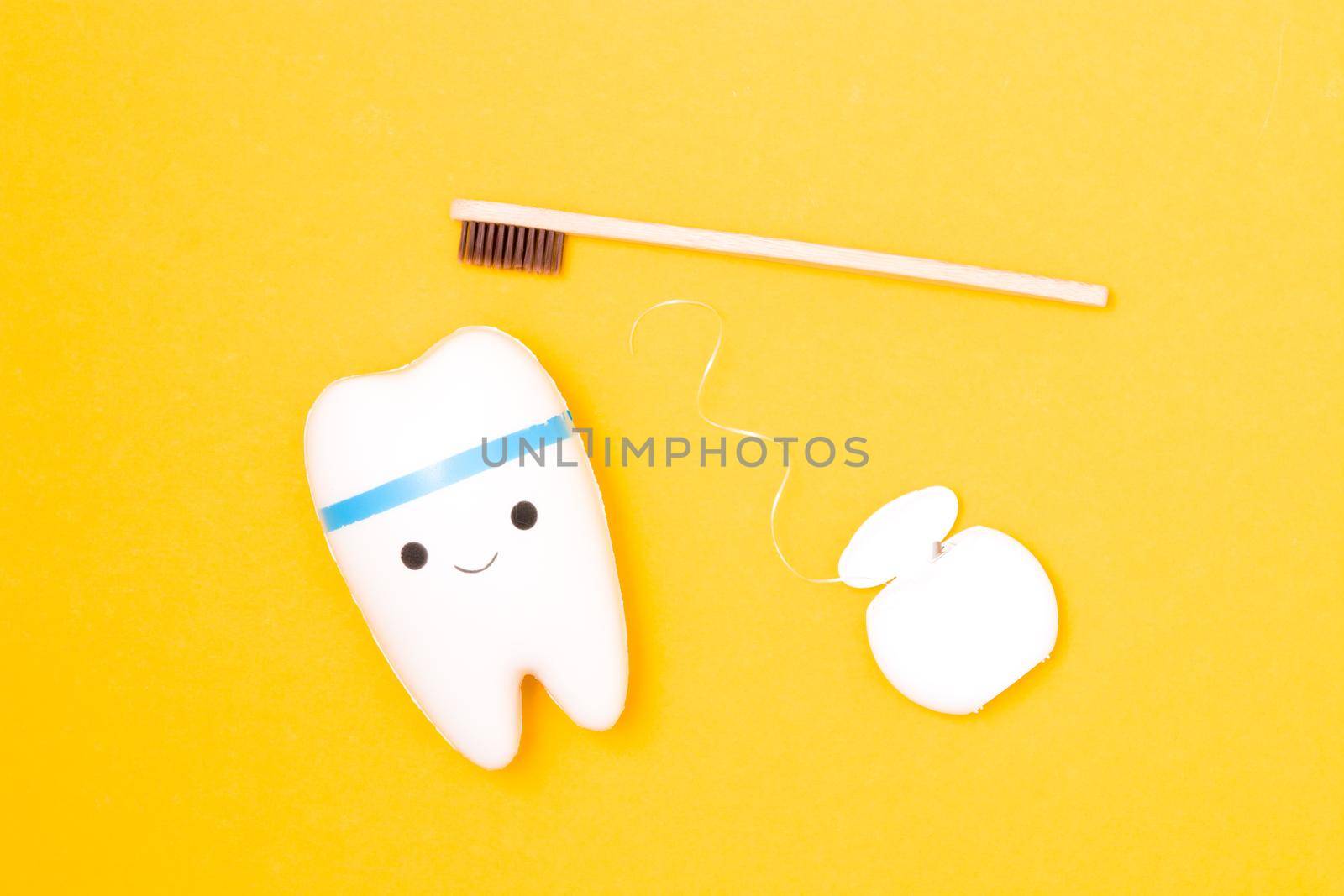 tooth model, dental floss and bamboo toothbrush on yellow background, happy tooth, white healthy tooth, copy space, oral care concept