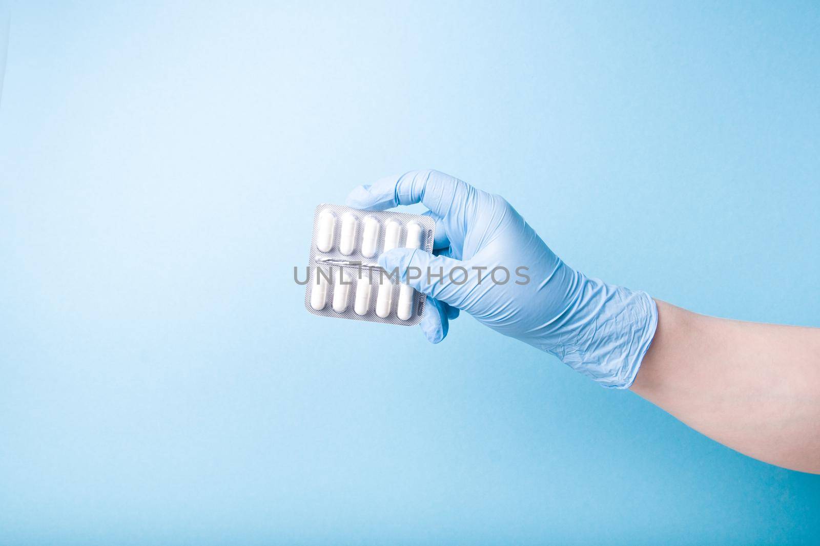 hand in a blue disposable medical glove holds a blister with green capsules blue background copy space by natashko