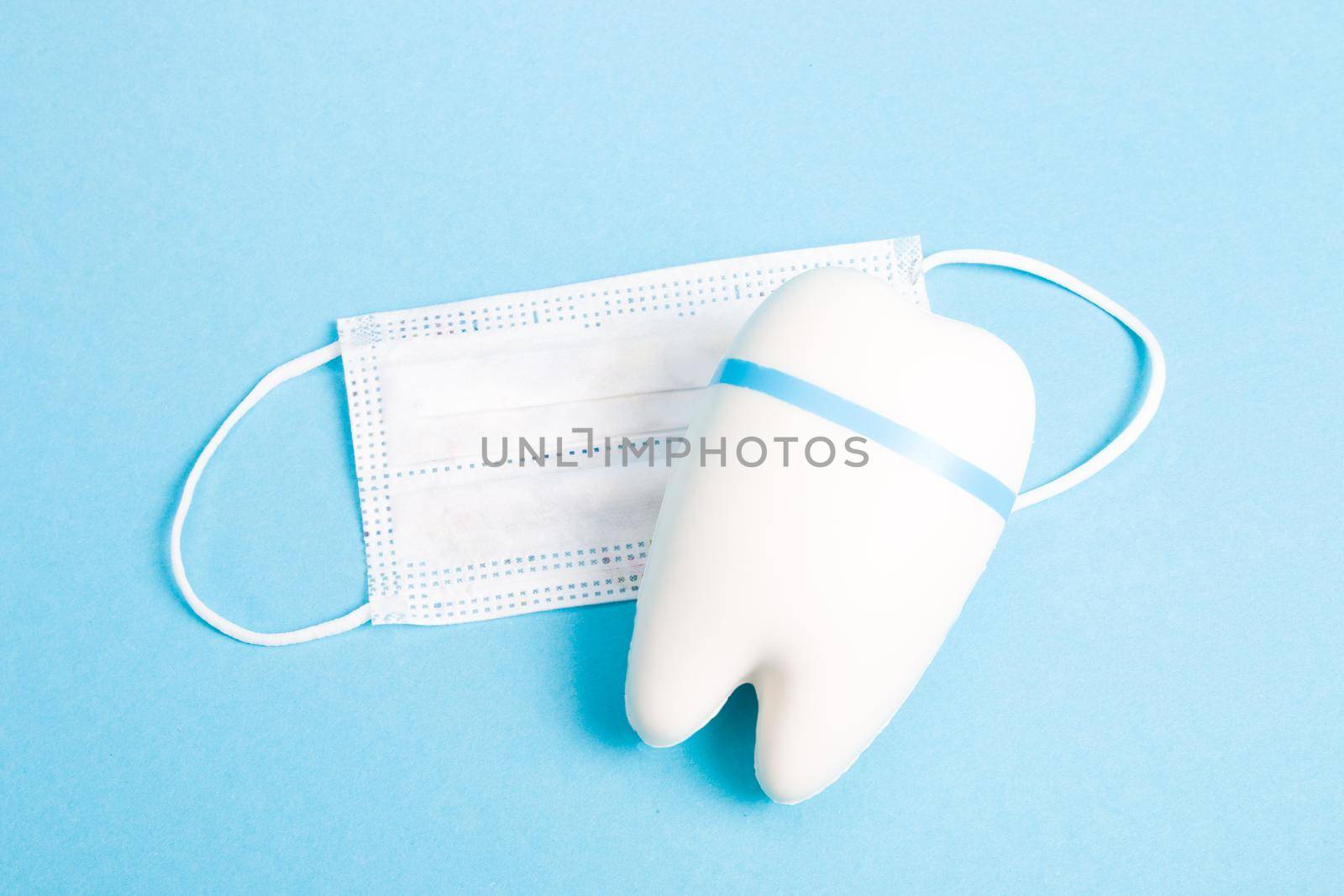 model of a sad white tooth and children's medical mask on a blue background copy space, dentistry concept, toothache dental treatment by natashko