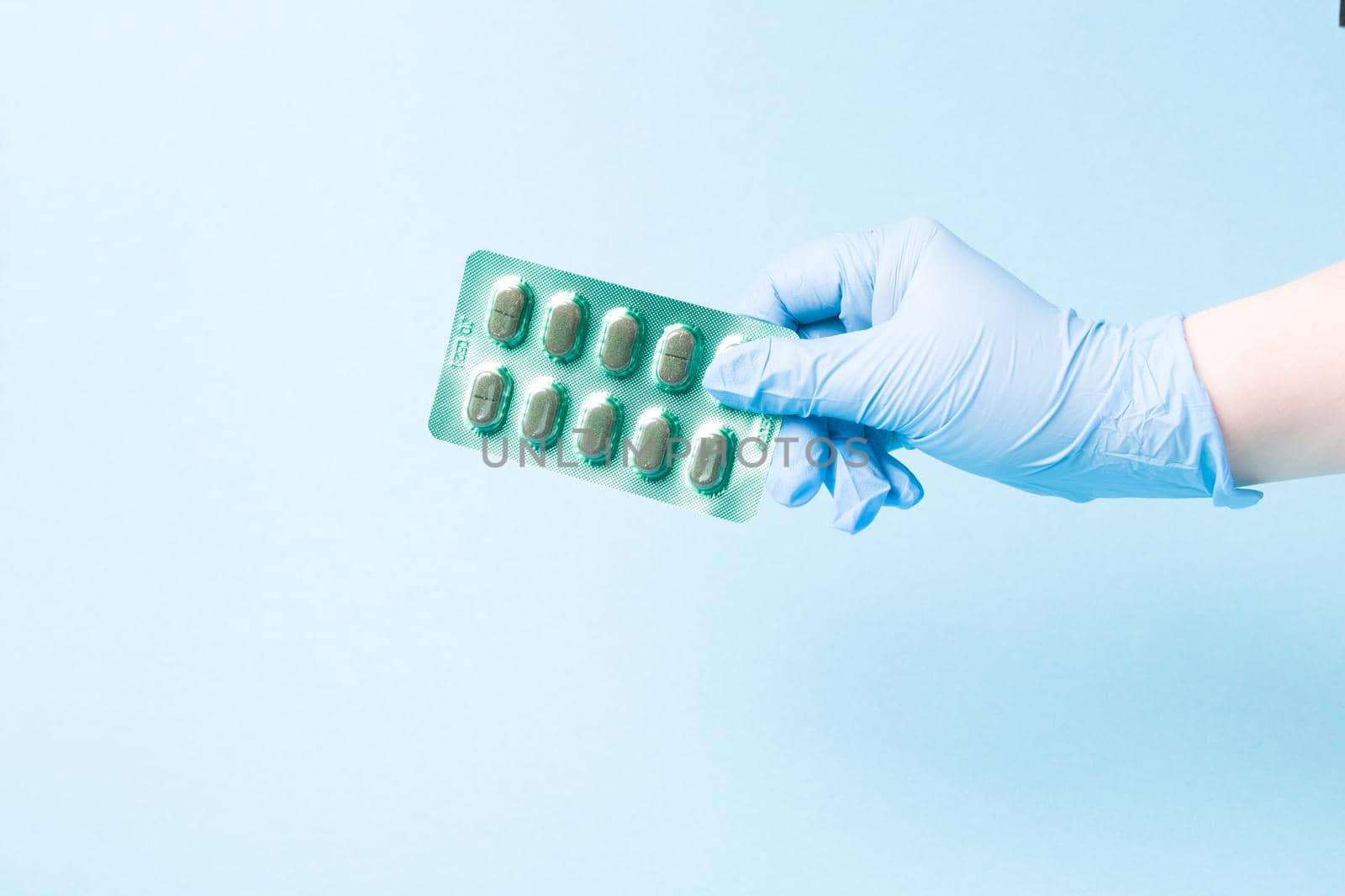 hand in a blue disposable medical glove holds a blister with green capsules blue background copy space