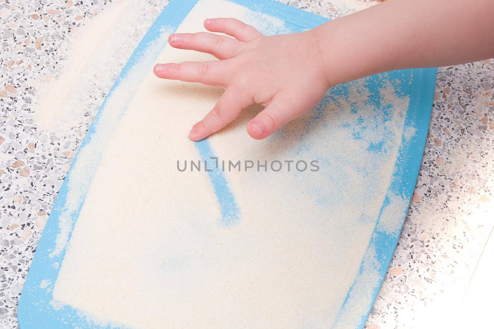 a small child draws a finger with semolina, a kitchen table, the development of fine motor skills, what to do with a child, cutting board blue by natashko