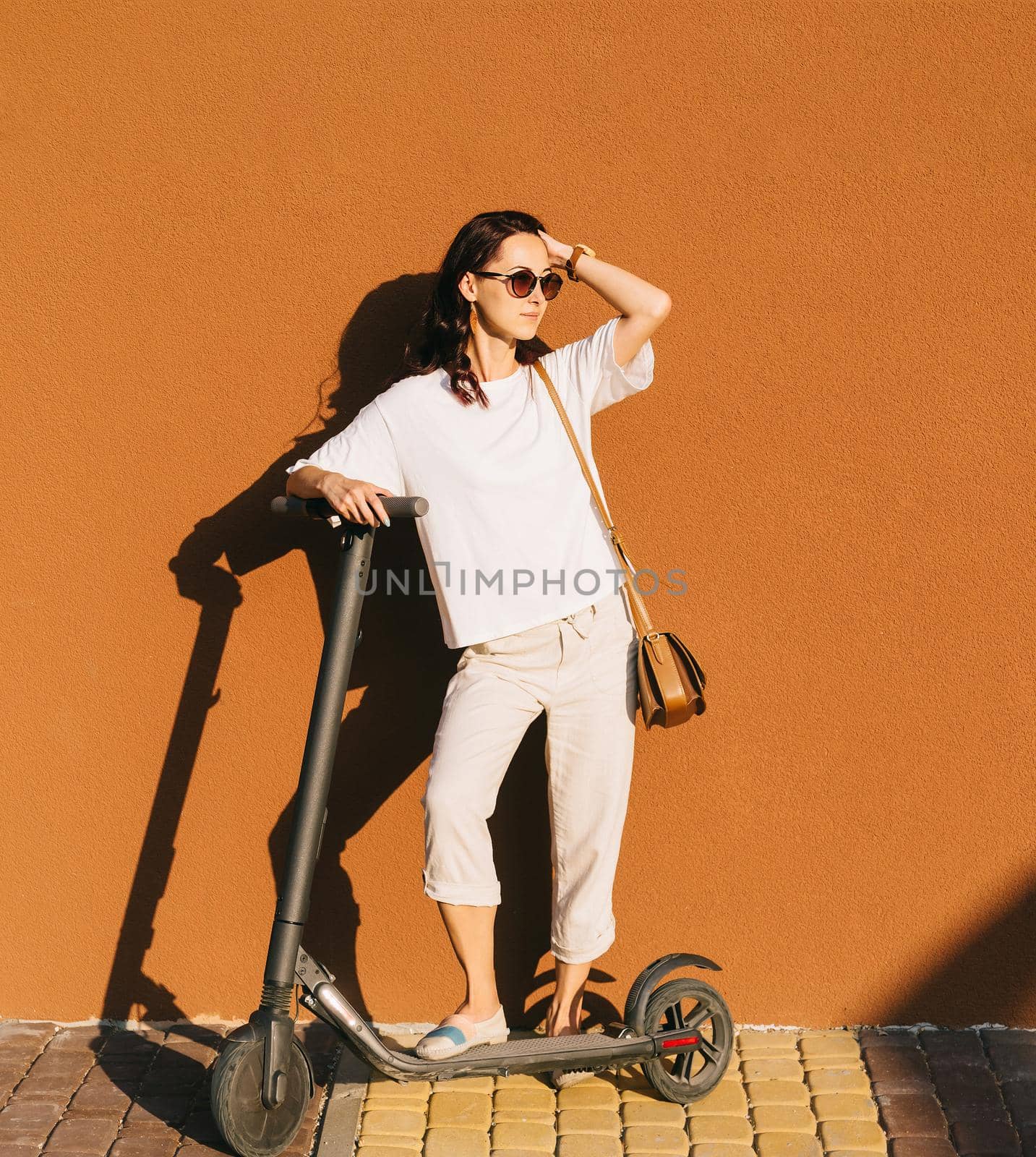 Beautiful young woman standing with electric scooter near the wall in street outdoor.