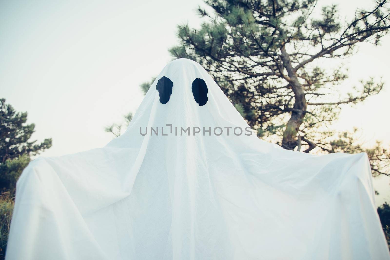 Spooky white ghost with black eyes walking in autumn forest. Halloween costume