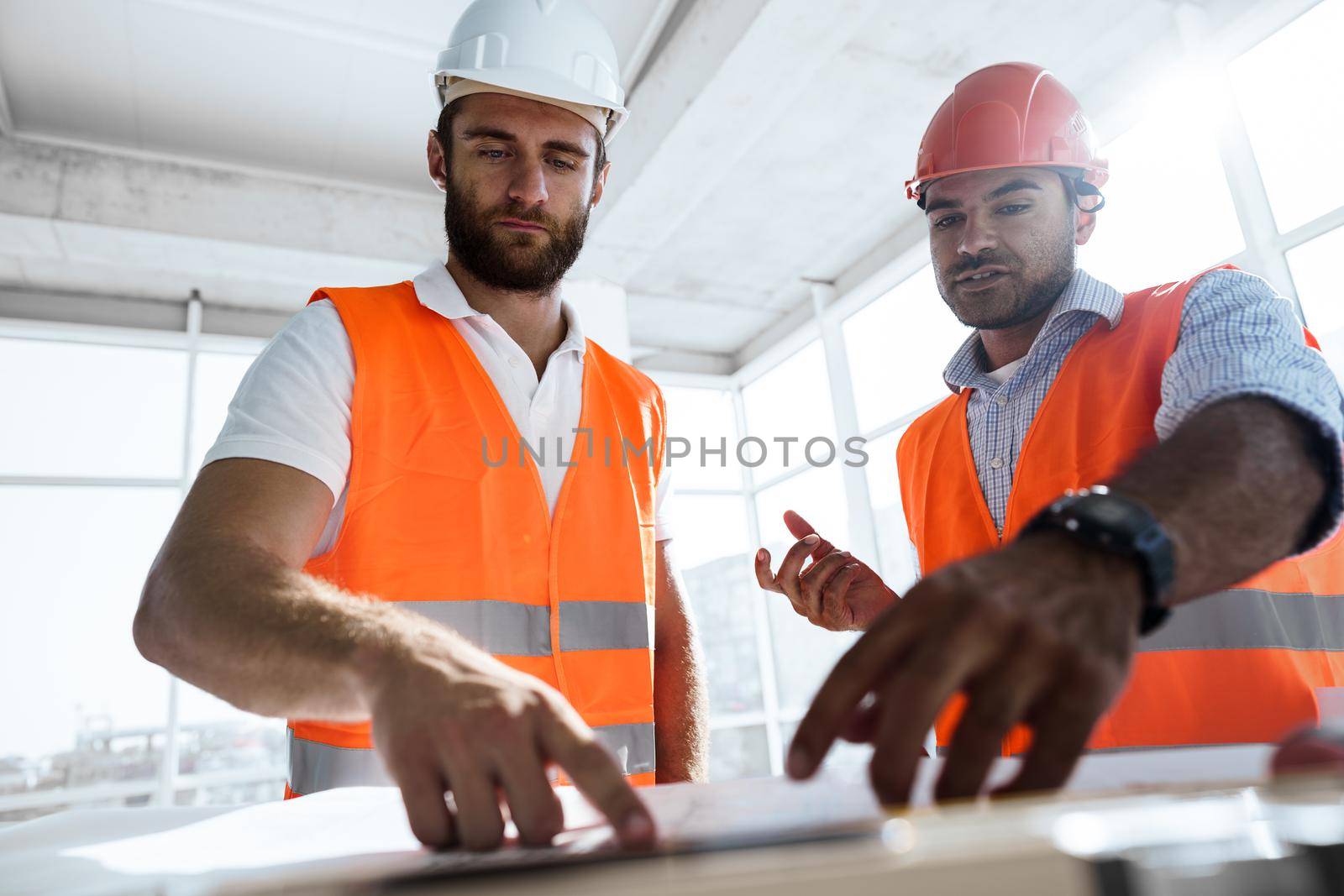 Two engineers man looking at project plan on the table in construction site by Fabrikasimf