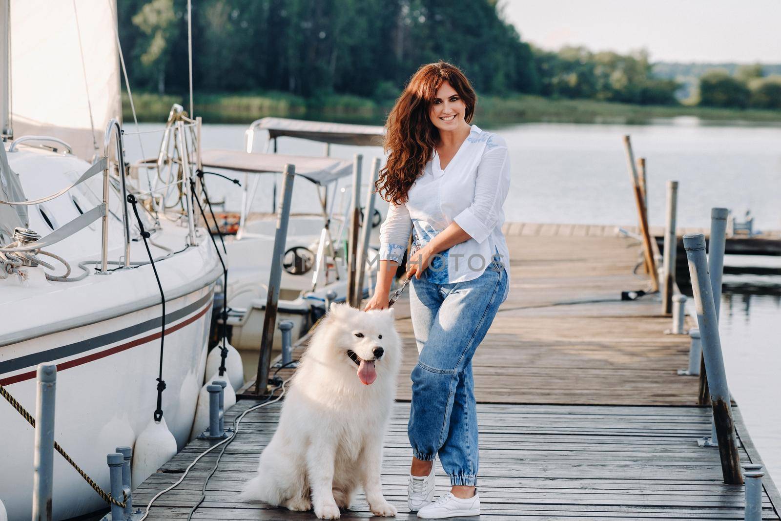 a happy woman with a big white dog stands on the pier near the yacht by Lobachad