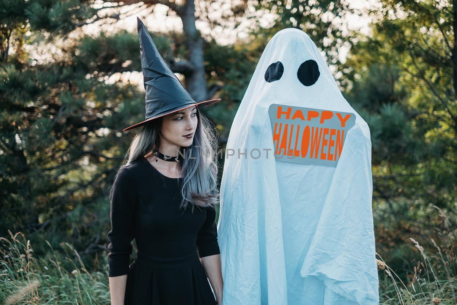 White ghost with empty poster and witch walking in autumn forest, free space. Halloween theme