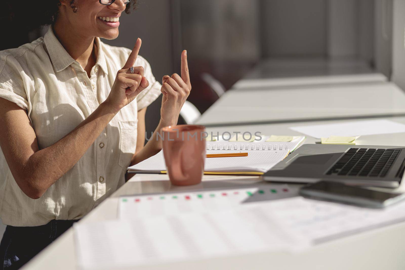 Smiling young lady learning and communicating in sign language online while sitting at workplace
