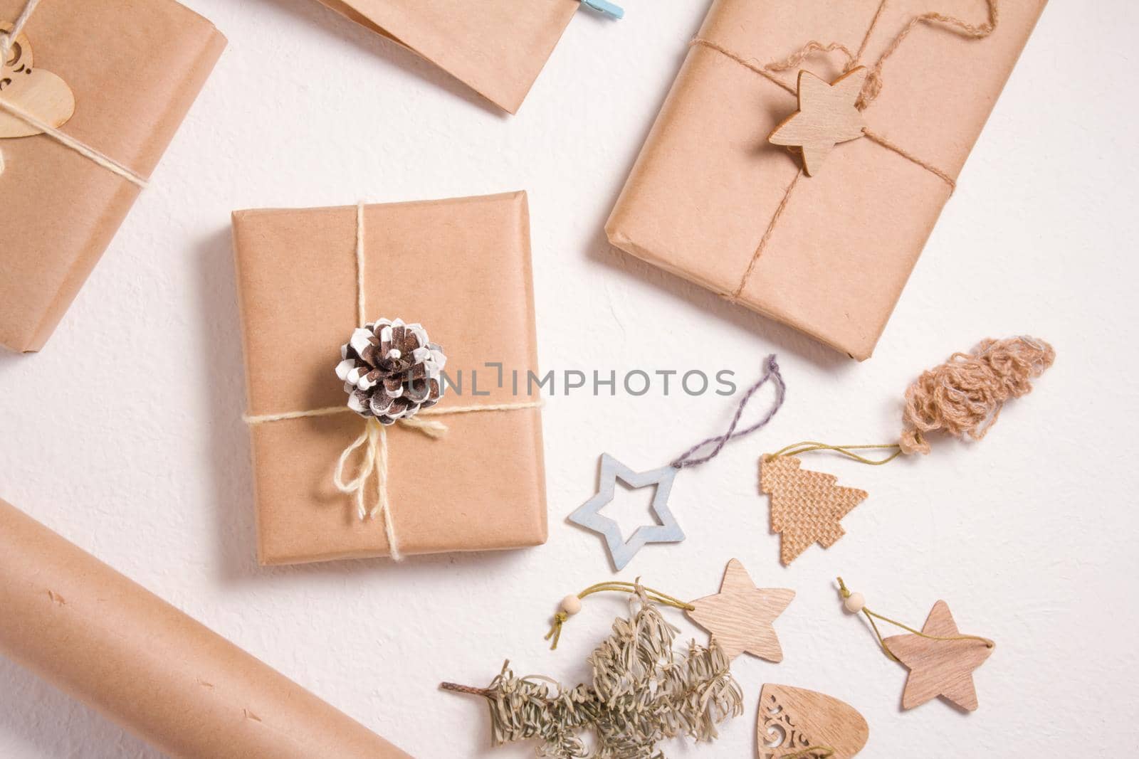 several gift wraps wrapped in kraft paper on a white background, eco friendly christmas concept, zero waste gifts, wooden christmas toys, a spruce branch and a pine cone on a white background