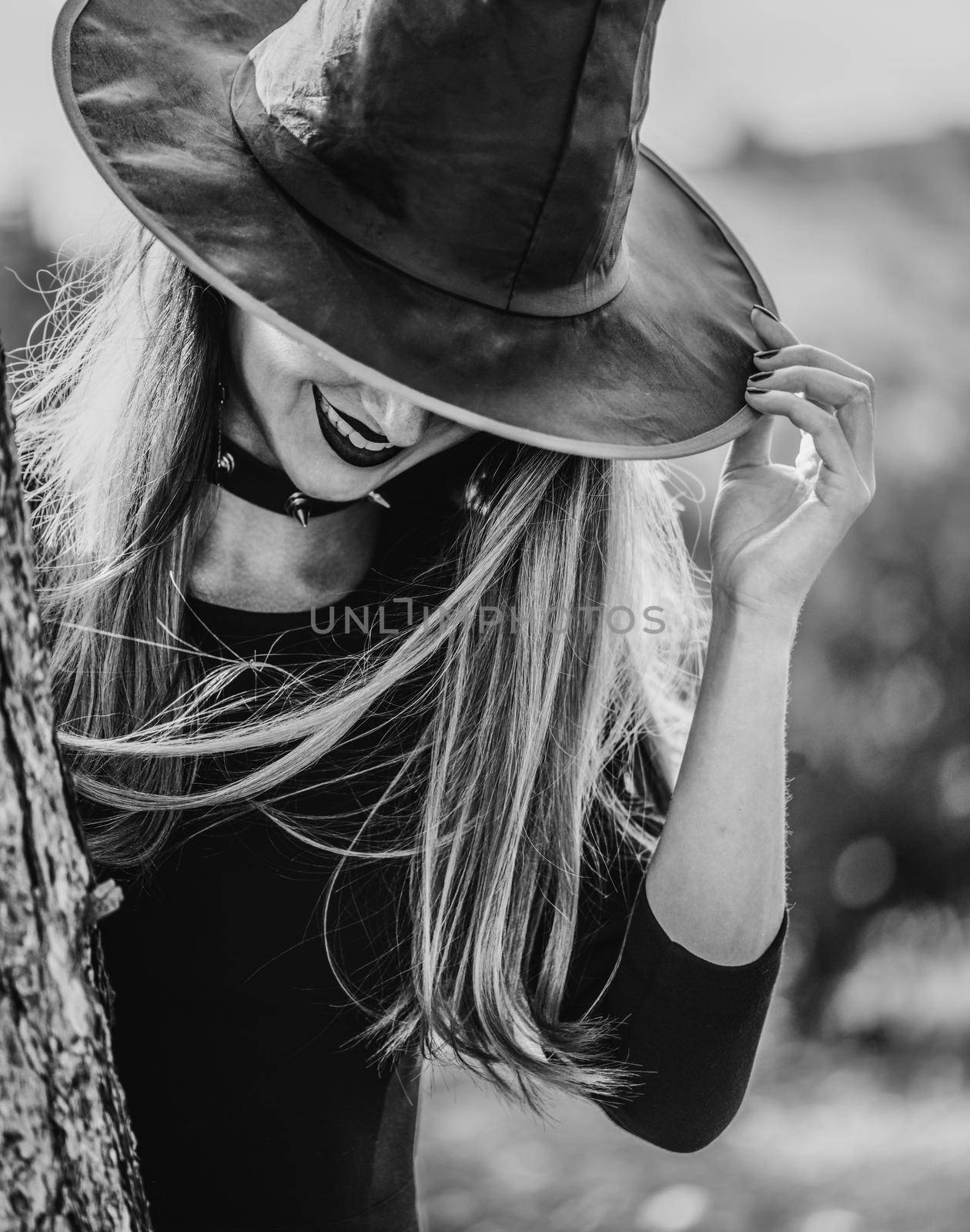 Scary young witch in a hat smiling outdoor. Theme of Halloween. Monochrome image