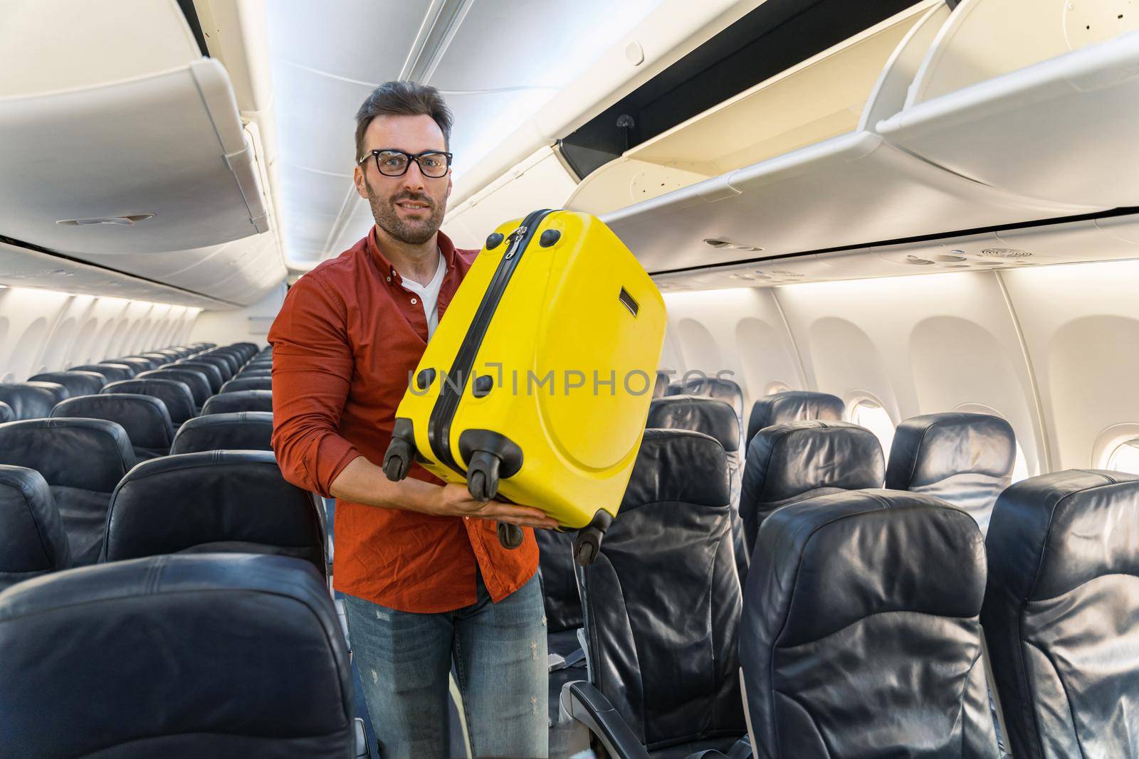 Happy male passenger wearing glasses holding yellow travel bag and looking at camera. Trip concept
