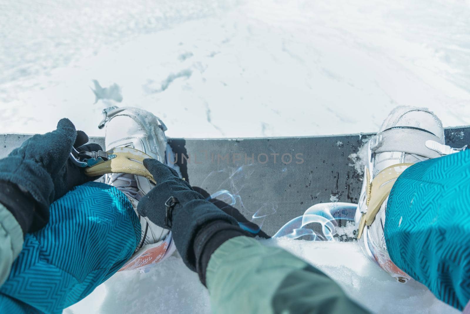 Unrecognizable man putting on his snowboard and tightening the straps on background of snow in winter, point of view