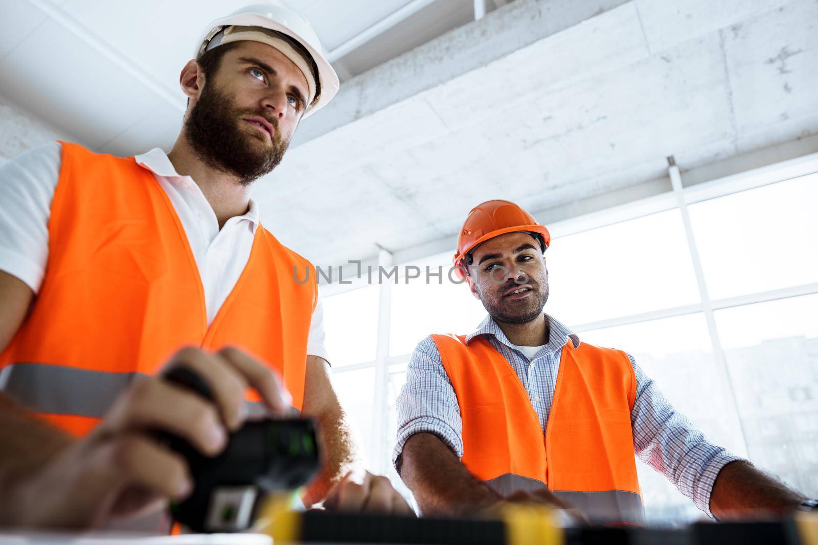 Portrait of two young construction engineers wearing hardhats working on construction site