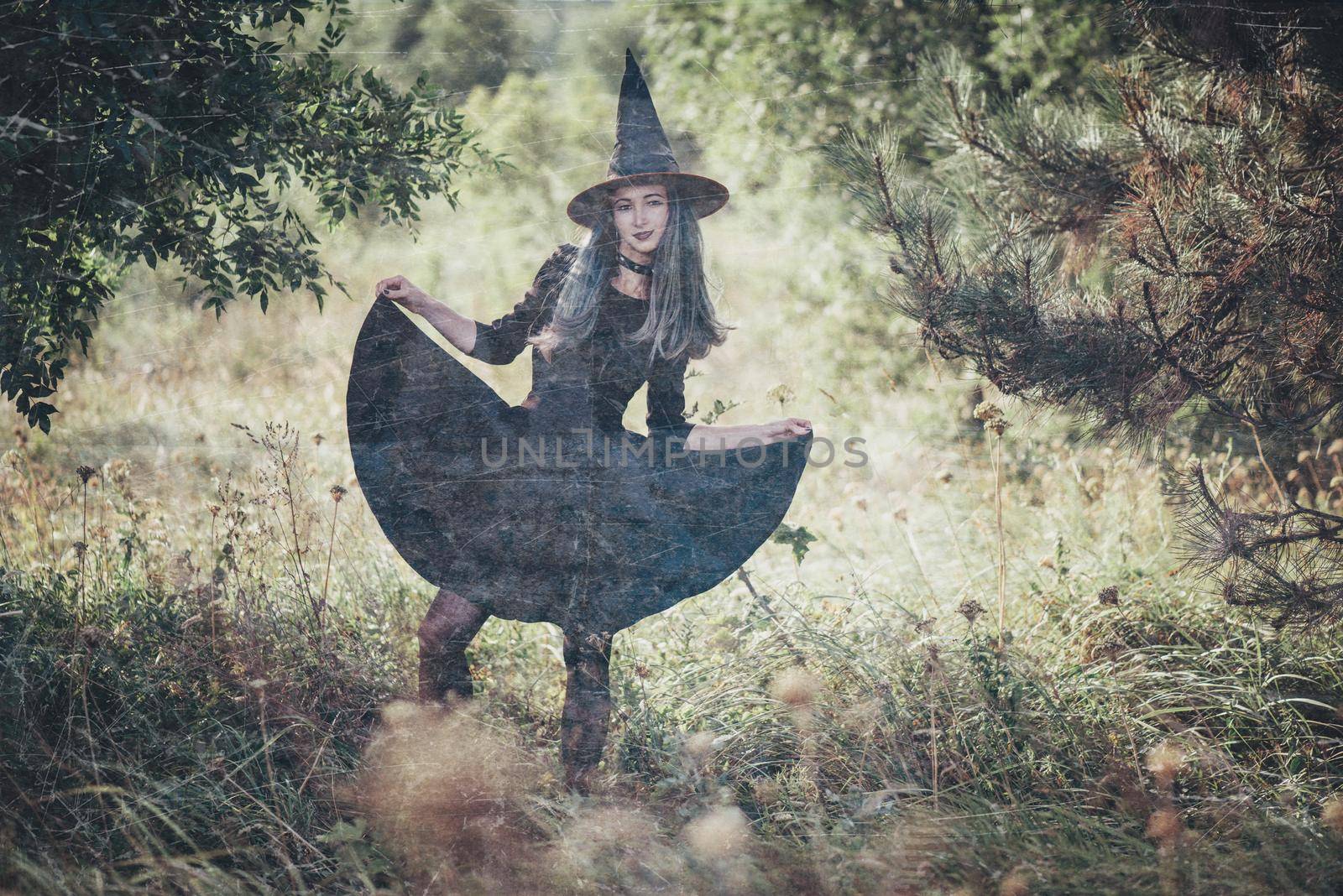 Young beautiful witch wearing in black dress and hat walking outdoor. Theme of Halloween and horror